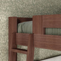 Close-up of walnut-finish solid wood bunk bed ladder and guardrail with green quilted bedding against vintage floral wallpaper