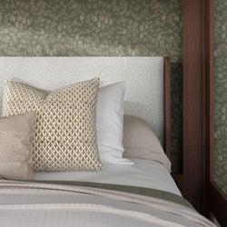Close-up of contemporary bedroom featuring an upholstered white headboard, patterned gold throw pillows, neutral linens, green floral wallpaper and dark wood frame
