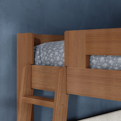 Close-up of wooden bunk bed ladder and guardrail in oak finish with blue floral bedding against a navy textured wall