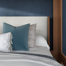 Close-up of decorative blue and patterned pillows on white bedding with textured headboard, navy accent wall, and wooden bedframe
