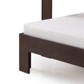 Close-up of white quilted mattress corner on dark wood platform bed frame with walnut-finish leg