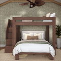 Modern wooden loft bunk bed with staircase and queen bed below, neutral bedding, woven ceiling fan and potted plant against green floral wallpaper