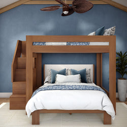Space-saving wooden loft bunk bed with staircase over queen bed, blue accent wall, patterned navy bedding, throw pillows and potted plant