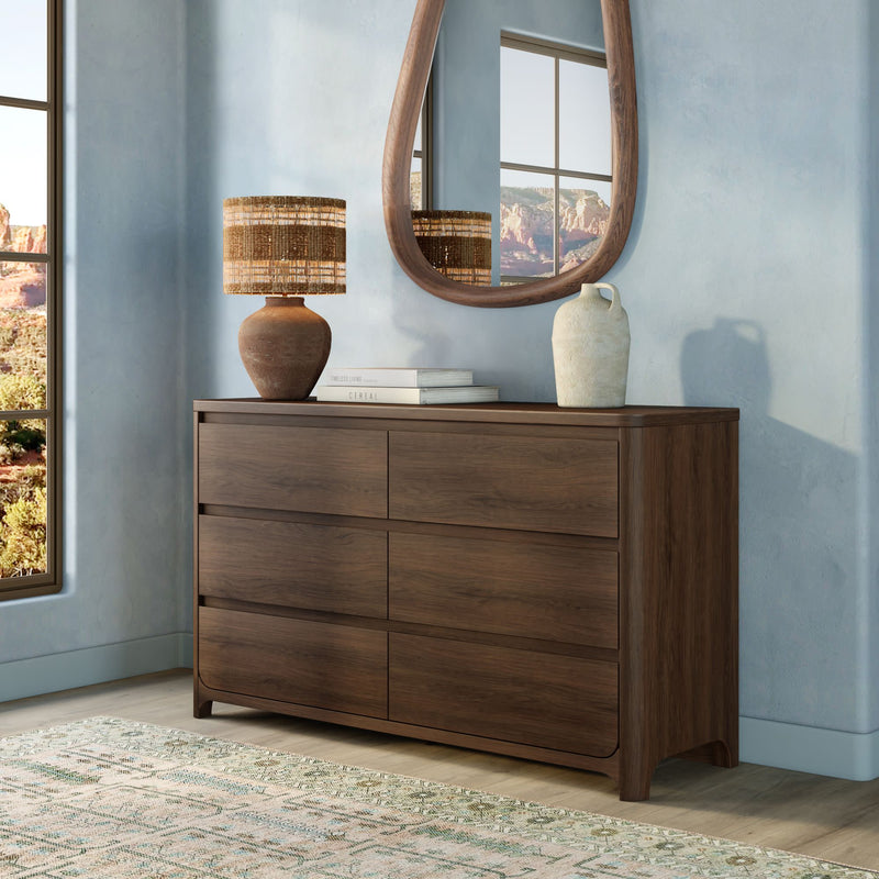 Walnut six-drawer wooden dresser in modern bedroom vignette with woven table lamp, oval mirror, ceramic vase, and desert view through window