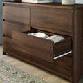 Walnut-finish wooden dresser with an open bottom drawer showing folded bedding and pillow, modern bedroom storage chest on hardwood floor with patterned rug
