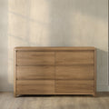 Natural oak 6-drawer dresser with rounded corners and minimalist design against a textured beige wall on hardwood floor