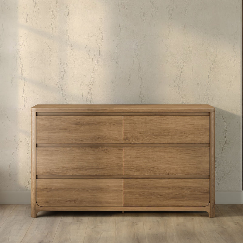 Natural oak 6-drawer dresser with rounded corners and minimalist design against a textured beige wall on hardwood floor