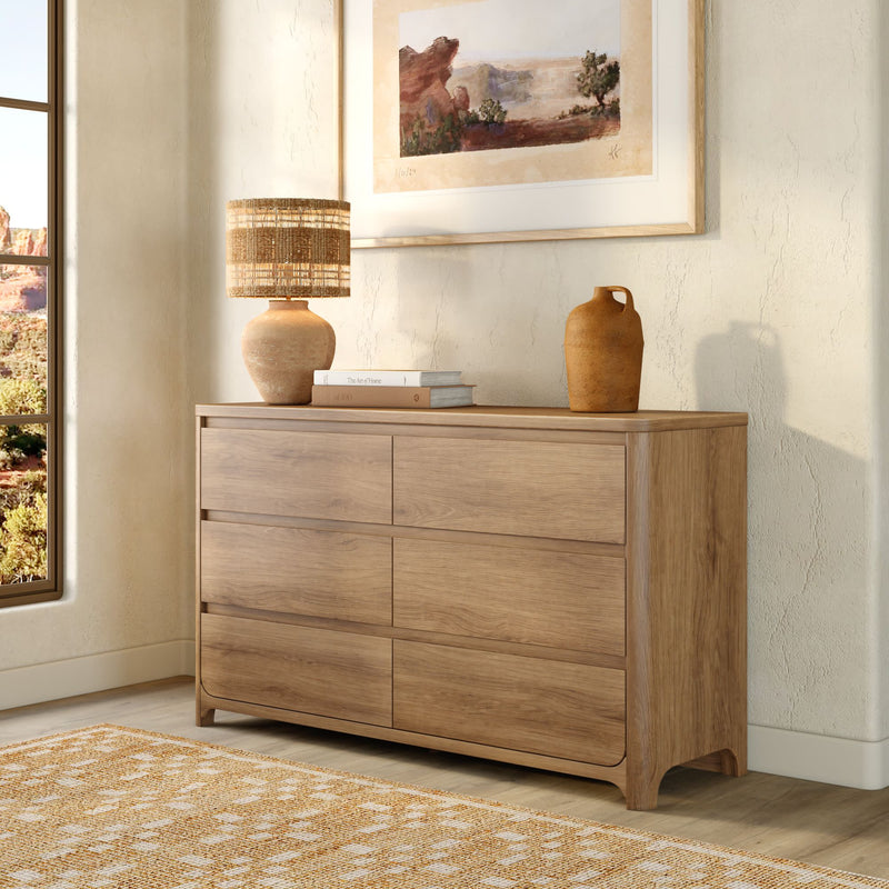 Light oak 6-drawer wooden dresser for bedroom storage styled with woven table lamp, ceramic vase, framed desert landscape art and jute rug