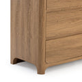 Close-up of modern bedroom dresser corner in natural oak finish showing rounded legs, horizontal wood-grain drawers and clean lines