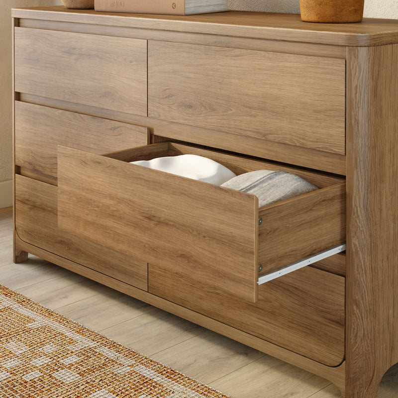 Modern oak-finish wooden dresser with open drawer revealing pillows — spacious bedroom storage on light hardwood floor with woven rug