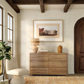 Modern rustic entryway with wooden six-drawer dresser, woven rattan table lamp, framed landscape art, arched wood door, neutral boho decor