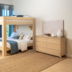 Light wood bunk bed and matching dresser in modern coastal bedroom with blue linens, woven jute rug, wall sconces and neutral decor
