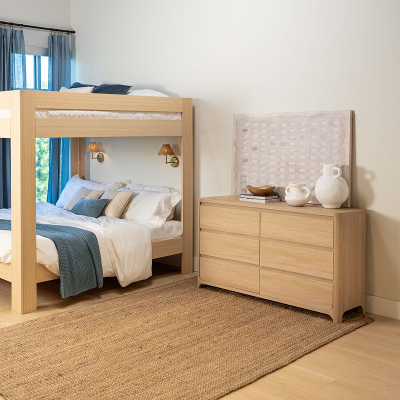 Light wood bunk bed and matching dresser in modern coastal bedroom with blue linens, woven jute rug, wall sconces and neutral decor