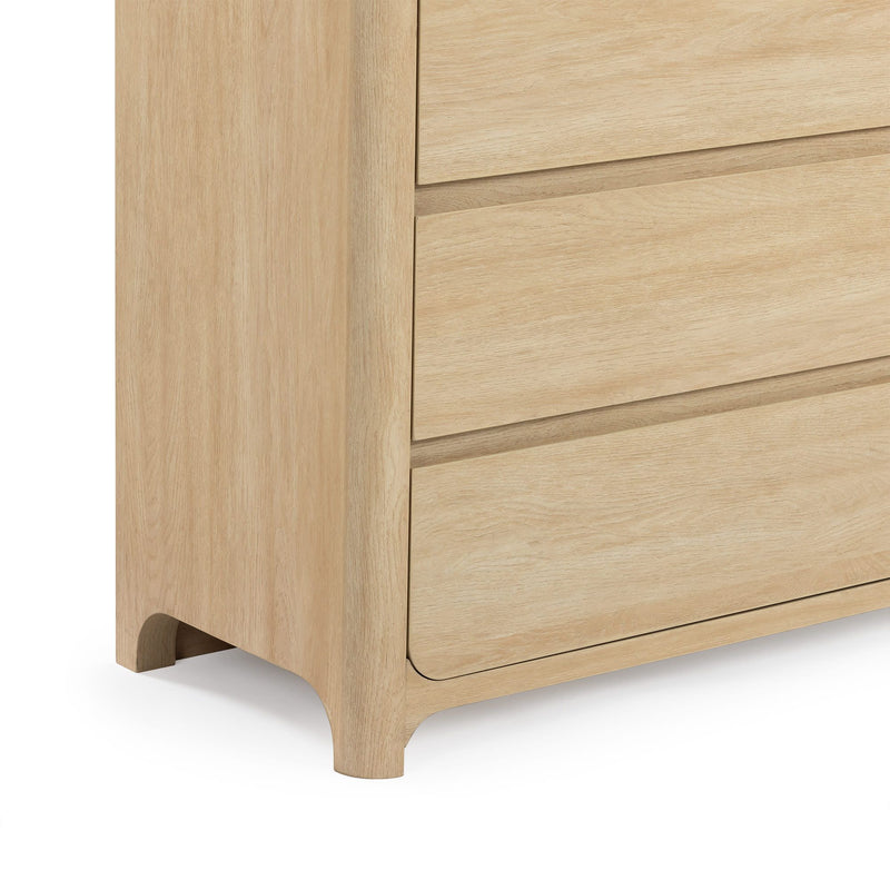 Close-up of light oak dresser corner with three drawers, rounded recessed feet and natural wood grain finish for modern bedroom furniture.