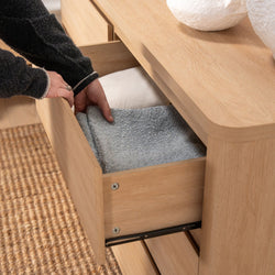 Hands placing a soft gray towel into an oak dresser drawer — minimalist bedroom linen storage and natural wood furniture