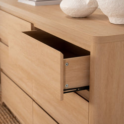 Light oak dresser with open drawer, rounded edges and visible wood grain topped with minimalist white ceramic vases — modern bedroom storage and natural oak finish