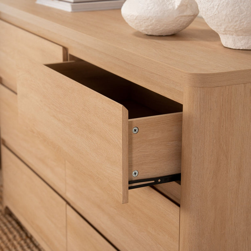 Light oak dresser with open drawer, rounded edges and visible wood grain topped with minimalist white ceramic vases — modern bedroom storage and natural oak finish