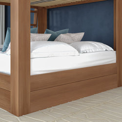 Wooden canopy bed with crisp white linens, patterned and teal accent pillows against a navy blue wall