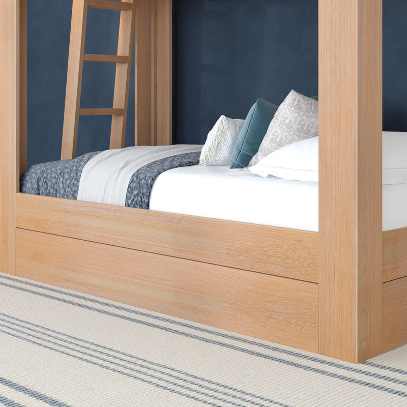 Light wood four-poster bed against a navy blue accent wall with white bedding, layered gray and blue throw blankets, patterned and solid decorative pillows, and a striped area rug in a coastal farmhouse bedroom