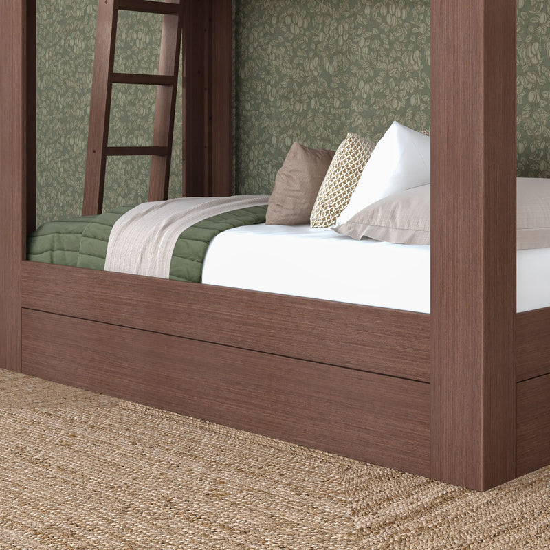 Close-up of a dark wood four-poster bed frame with a green quilt, beige throw and decorative pillows against patterned green wallpaper over a natural jute rug