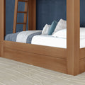 Modern wooden four-poster canopy bed with blue-and-white layered bedding, decorative throw pillows and textured cream area rug against a navy accent wall
