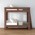 Modern solid wood twin-over-twin bunk bed with angled ladder, green and beige bedding and pillows on hardwood floor
