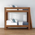 Modern wooden twin-over-twin bunk bed with blue and white bedding, decorative pillows and ladder on hardwood floor in minimalist bedroom