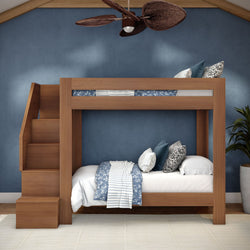 Modern wooden twin-over-twin bunk bed with built-in stairs in a blue-walled bedroom, white and blue patterned bedding and decorative pillows, ceiling fan and potted plant — space-saving kids' room design.