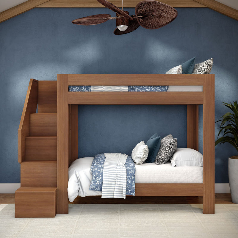 Modern wooden twin-over-twin bunk bed with built-in stairs in a blue-walled bedroom, white and blue patterned bedding and decorative pillows, ceiling fan and potted plant — space-saving kids' room design.
