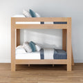 Modern light oak twin-over-twin bunk bed with blue and white bedding and decorative pillows in a minimalist bedroom on hardwood flooring