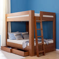 Wooden bunk bed with ladder and pull-out under-bed storage in blue bedroom, styled with gray and blue pillows on light hardwood floor