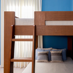 Wood bunk bed with ladder against blue accent wall, white curtains, neutral quilted bedding and gray-blue striped throw pillows