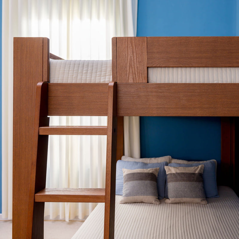 Wood bunk bed with ladder against blue accent wall, white curtains, neutral quilted bedding and gray-blue striped throw pillows