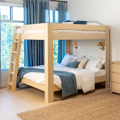 Modern light-wood bunk bed with ladder, white bedding and blue throw in bright minimalist kids' bedroom with blue curtains and natural jute rug