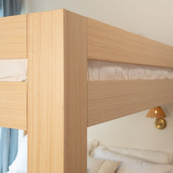 Close-up of light oak bunk bed corner, wooden bed frame with natural wood grain and white bedding in a modern minimalist bedroom