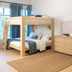 Modern light wood bunk bed with ladder in bright kids' bedroom, white bedding and blue throw, blue curtains, woven jute rug and wooden dresser