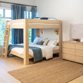 Modern light wood bunk bed with ladder in bright kids' bedroom, white bedding and blue throw, blue curtains, woven jute rug and wooden dresser