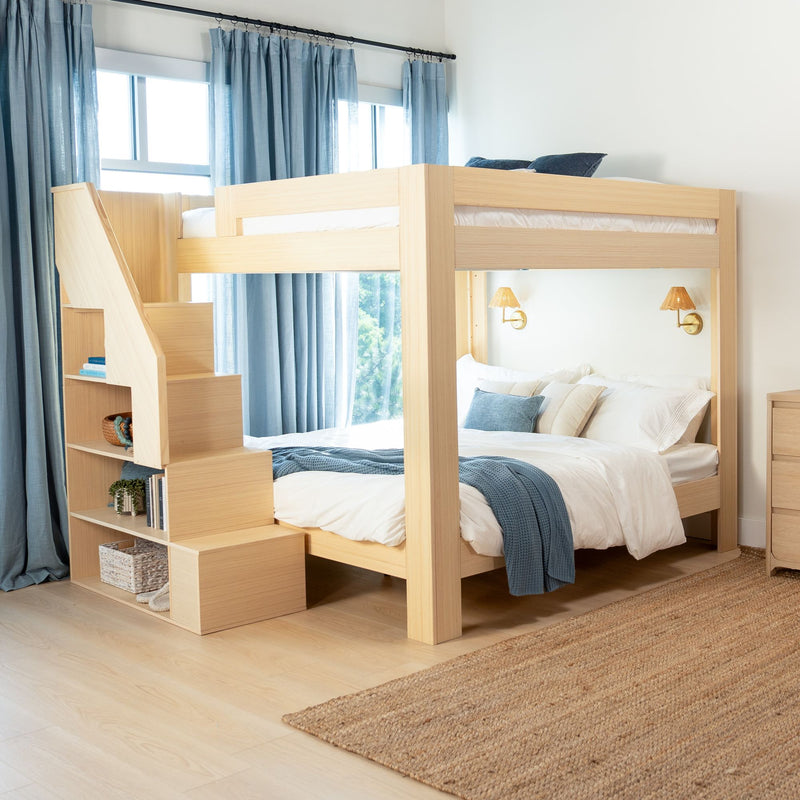 Modern light wood bunk bed with built-in storage stairs in bright bedroom with blue curtains, white bedding, navy throw and brass wall sconces