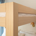Close-up of light oak bunk bed frame corner showing natural wood grain, minimalist modern bedroom design and white bedding