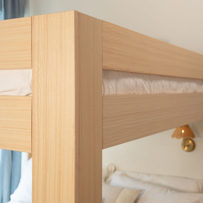 Close-up of light oak bunk bed frame corner showing natural wood grain, minimalist modern bedroom design and white bedding