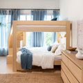 Modern natural wood loft bunk bed in a bright coastal-inspired bedroom with white bedding, blue curtains, woven jute rug and wooden dresser