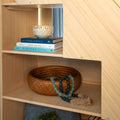 Light oak shelf styled for coastal home decor with a woven wicker basket, blue-green beaded garland, candle in a rattan holder and stacked coastal books (Waterside Living, Sailing the Seas, Patterns of Portugal)