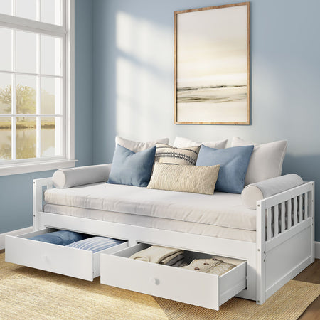 White wooden daybed with two pull-out storage drawers, beige mattress and blue-and-neutral decorative pillows in a light-blue modern coastal bedroom with framed abstract art and sunlight from a window