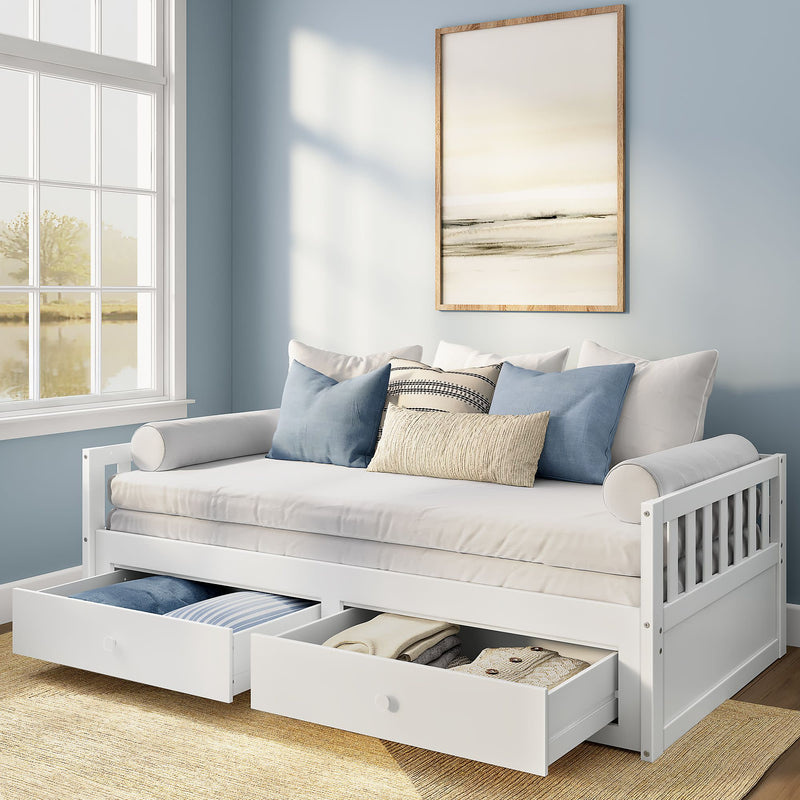 White wooden daybed with two pull-out storage drawers, beige mattress and blue-and-neutral decorative pillows in a light-blue modern coastal bedroom with framed abstract art and sunlight from a window