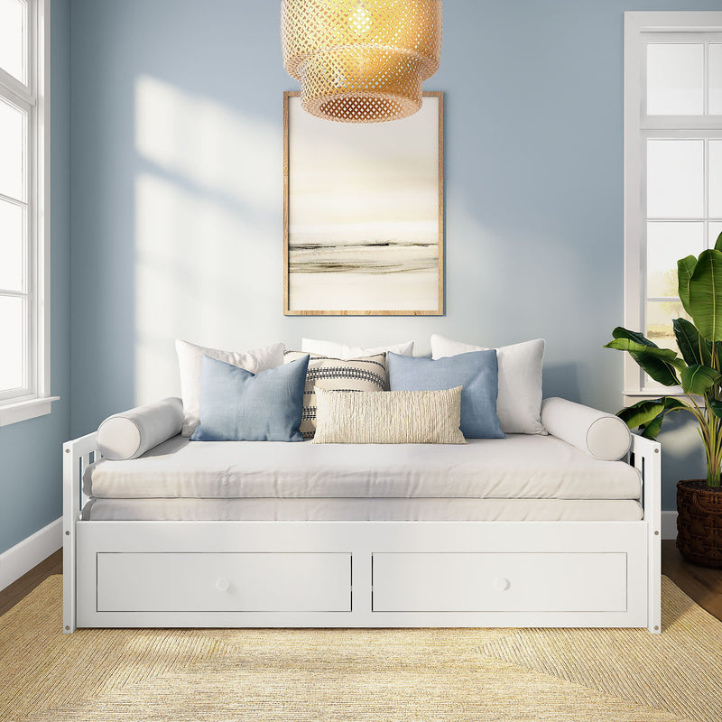 White wooden daybed with built-in storage drawers, layered neutral and blue throw pillows, light blue walls, framed coastal artwork, woven rattan pendant light and potted plant in a bright sunlit coastal farmhouse living room