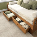 Wooden daybed with pull-out storage drawers, beige linen mattress and green accent pillows on textured rug — space-saving bedroom furniture
