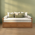 Wooden daybed with storage drawers, cream cushions and olive-green throw pillows against a sage-green wall in a minimalist cozy living room