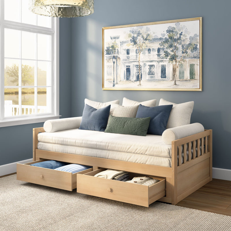 Light wood daybed with under-bed storage drawers, cream mattress and blue and green throw pillows in a cozy blue-gray living room with framed watercolor wall art and a large window letting in natural light
