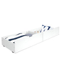 White wooden underbed trundle storage drawer with navy-striped bedding and blue letter pillow, low-profile roll-out organizer for kids' bedroom
