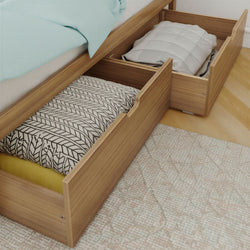 Wooden underbed storage drawers open beneath a bed with folded blankets and pillows — space-saving bedroom storage solution